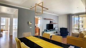 A modern living room with a dining area, a TV, and a balcony with a city view. - Lido Life Apartment by LovelyStay (Funchal)