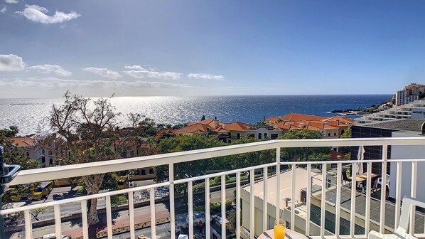 A balcony with a view of the sea, buildings, and a clear sky.