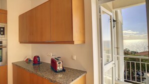 A kitchen with wooden cabinets, a granite countertop, a toaster, and a kettle. - Lido Life Apartment by LovelyStay (Funchal)