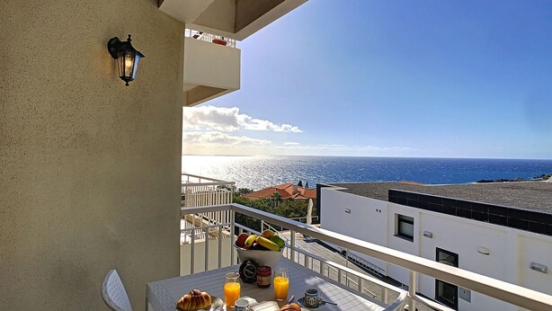 A balcony with a table set for breakfast, overlooking a coastal view. - Lido Life Apartment by LovelyStay (Funchal)