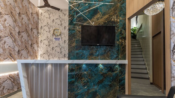 Zona de recepción con pared de mármol, televisor montado y escalera que sube a otro nivel.