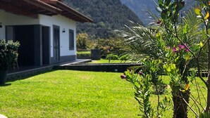 A house with a white exterior and a red roof, surrounded by a well-maintained lawn and a garden with various plants and flowers.