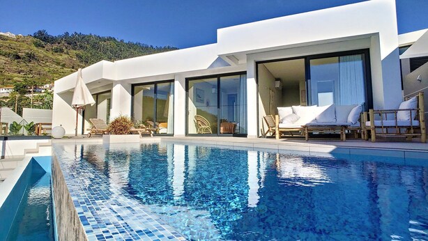A modern pool area with clear blue water, sun loungers, and a view of a hillside. - Noah - Private Sunset Hideaway (Arco Da Calheta)