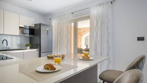 Cocina moderna con espacio para desayunar, que incluye croissants y jugo de naranja, y vista a un edificio de piedra por la ventana.