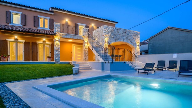 Una casa de dos pisos con piscina, fachada de piedra y zona de estar al aire libre.