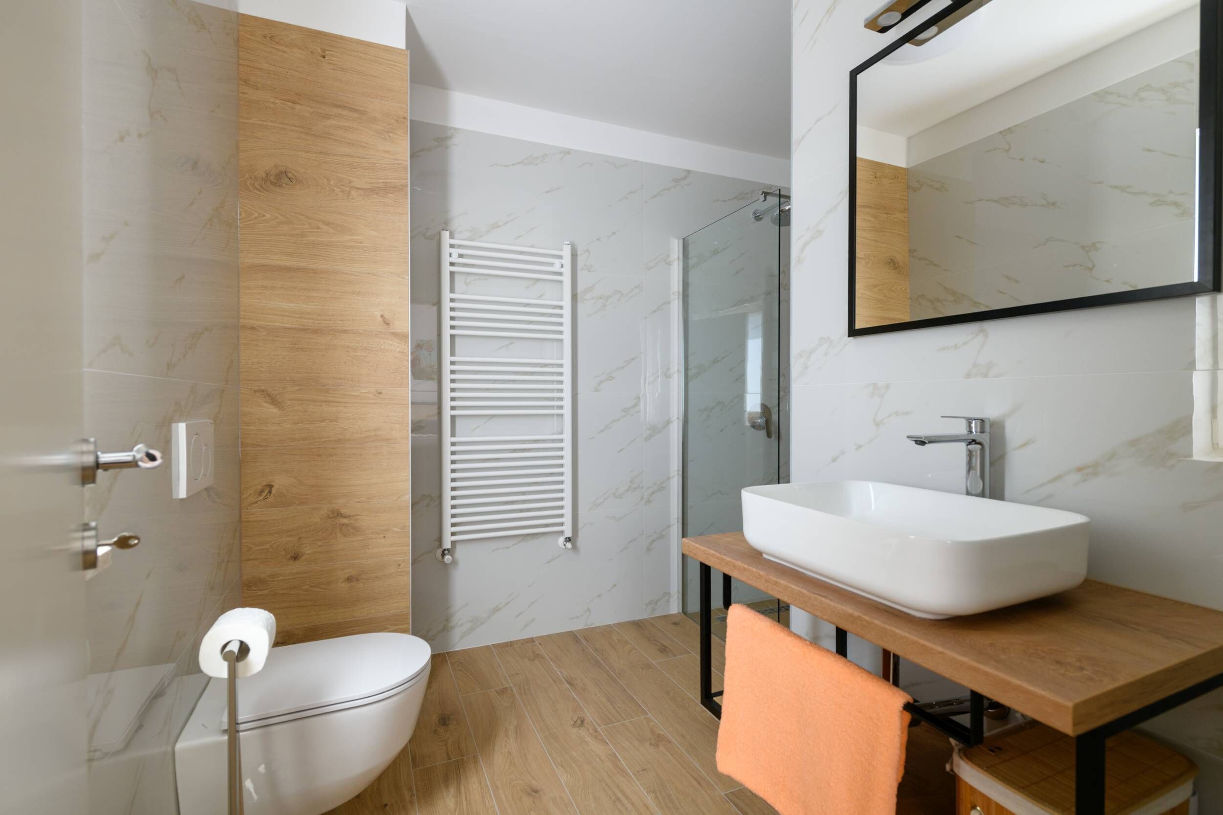 Ein modernes Badezimmer mit einer weißen Toilette, einem Holzkosmetikschrank mit Waschbecken und einer Duschkabine aus Glas.