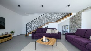 Una sala de estar moderna con una escalera, dos sofás morados, una mesa de centro de madera y una pared de acento de piedra.