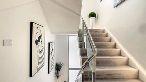 Eine moderne Treppe mit Holzboden und Glasgeländer, die zu einer Zwischenebene mit einer Tür führt.