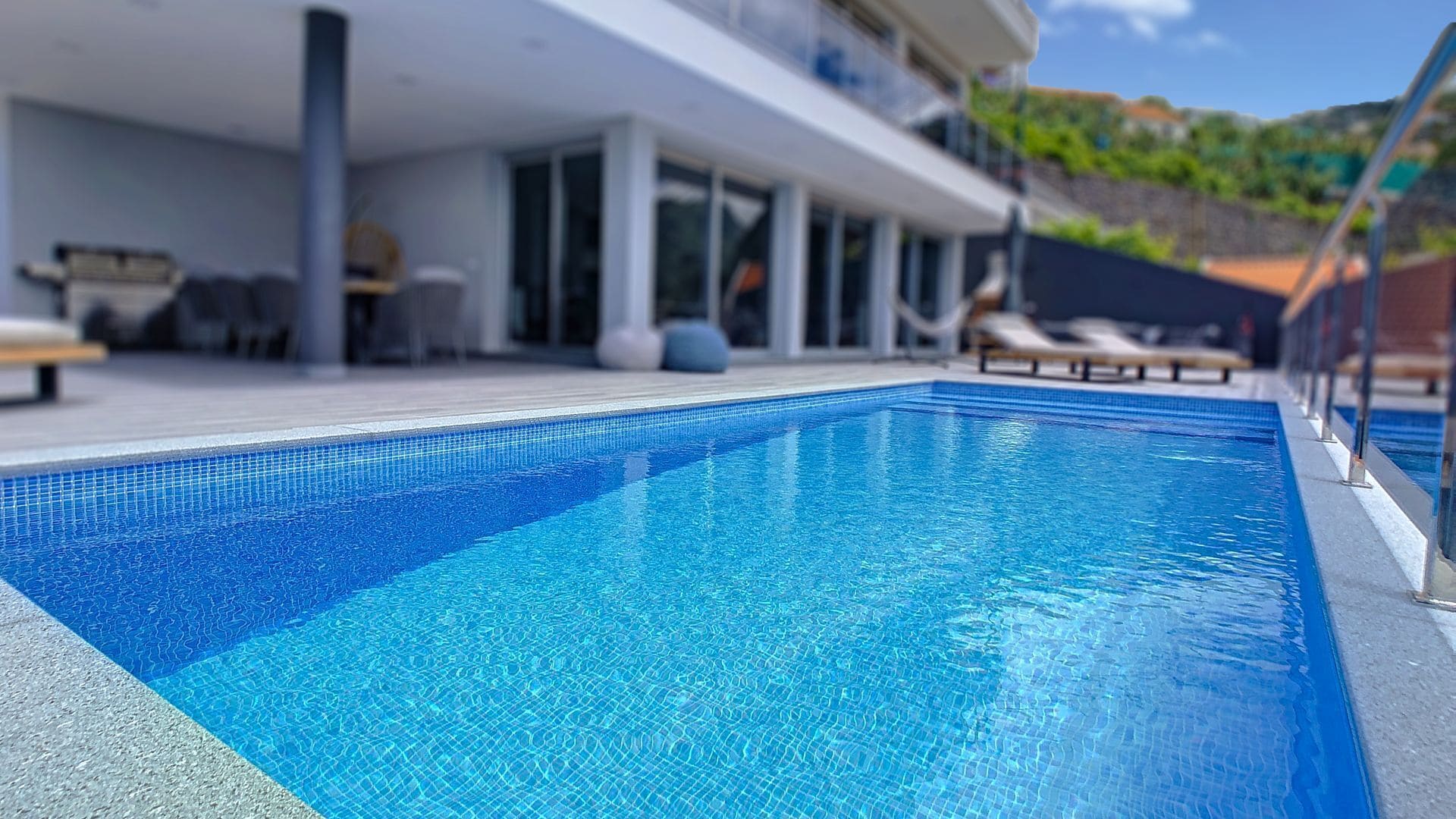 A modern pool area with a clear blue pool, lounge chairs, and a building with large windows.