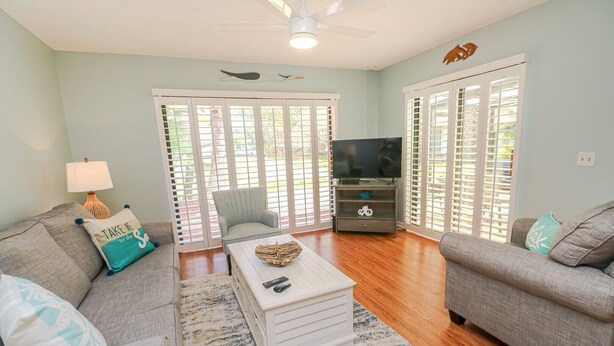 A living room with two sofas, a coffee table, a TV stand, and a ceiling fan.