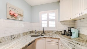 A kitchen with a marble countertop, a sink, a coffee maker, and a window with blinds.