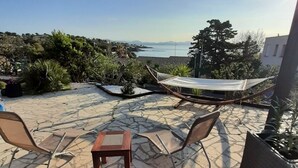 Una terraza de madera con una mesa y sillas, con vistas panorámicas al mar y las colinas.