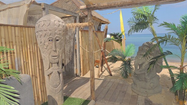 Una zona junto a la playa con esculturas de piedra, una terraza de madera y una estructura con techo de paja.