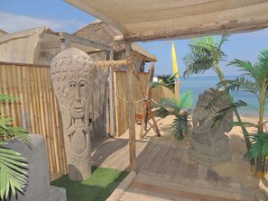 A beachside area with stone sculptures, a wooden deck, and a thatched-roof structure.