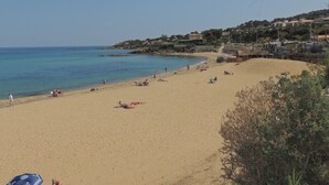 Una playa con cielos despejados, gente tomando el sol y edificios al fondo.