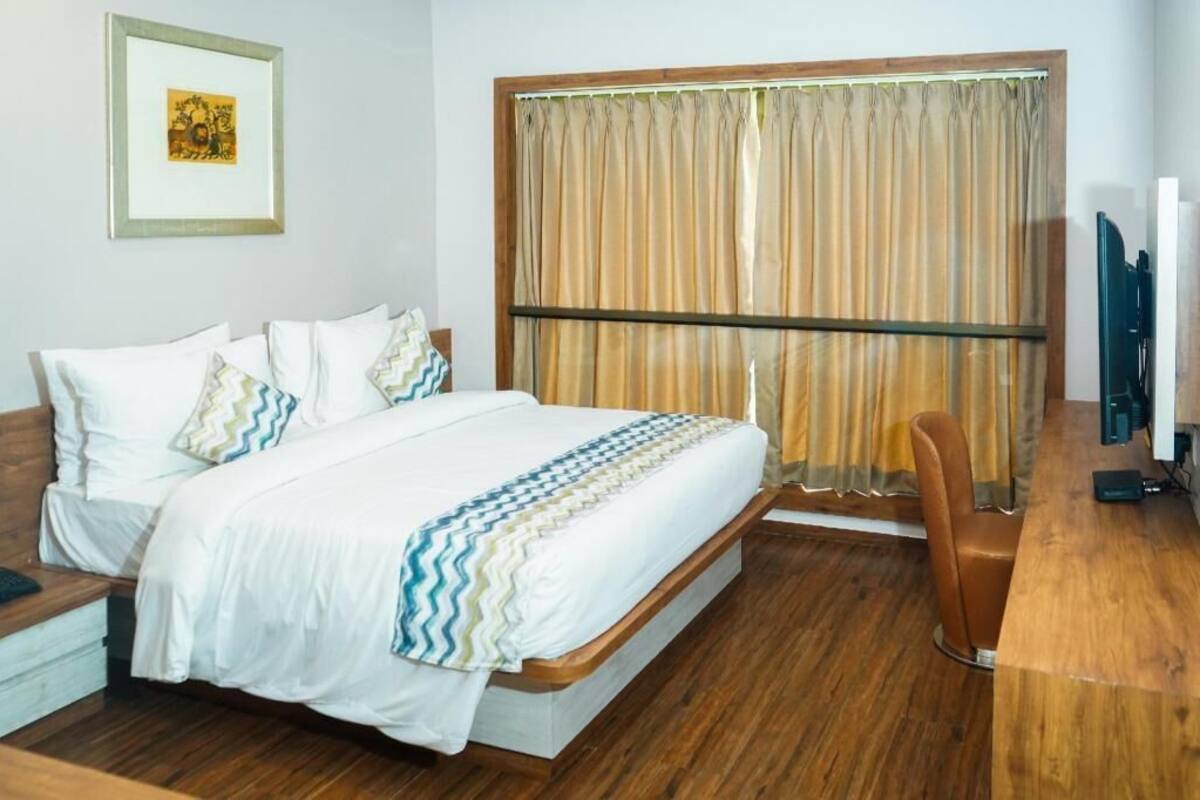 Ein Hotelzimmer mit Bett, Schreibtisch, Stuhl, Fernseher und einem Fenster mit Vorhängen.