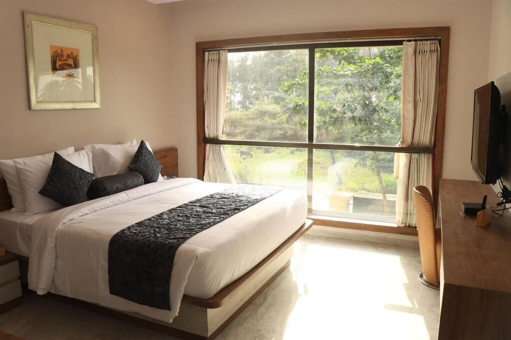 A bedroom with a large bed, a TV, a desk, and a window with curtains.