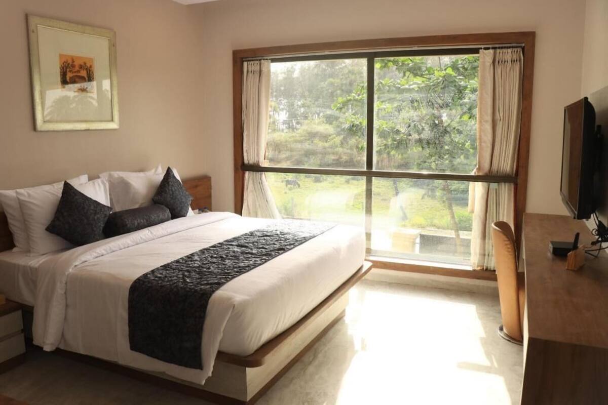 Ein Schlafzimmer mit einem großen Bett, einem Fernseher, einem Schreibtisch und einem Fenster mit Vorhängen.