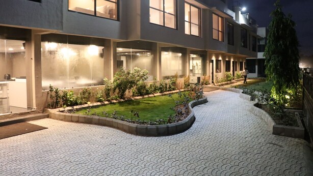 Un hotel moderno con un patio que cuenta con un sendero pavimentado, vegetación y ventanas iluminadas.