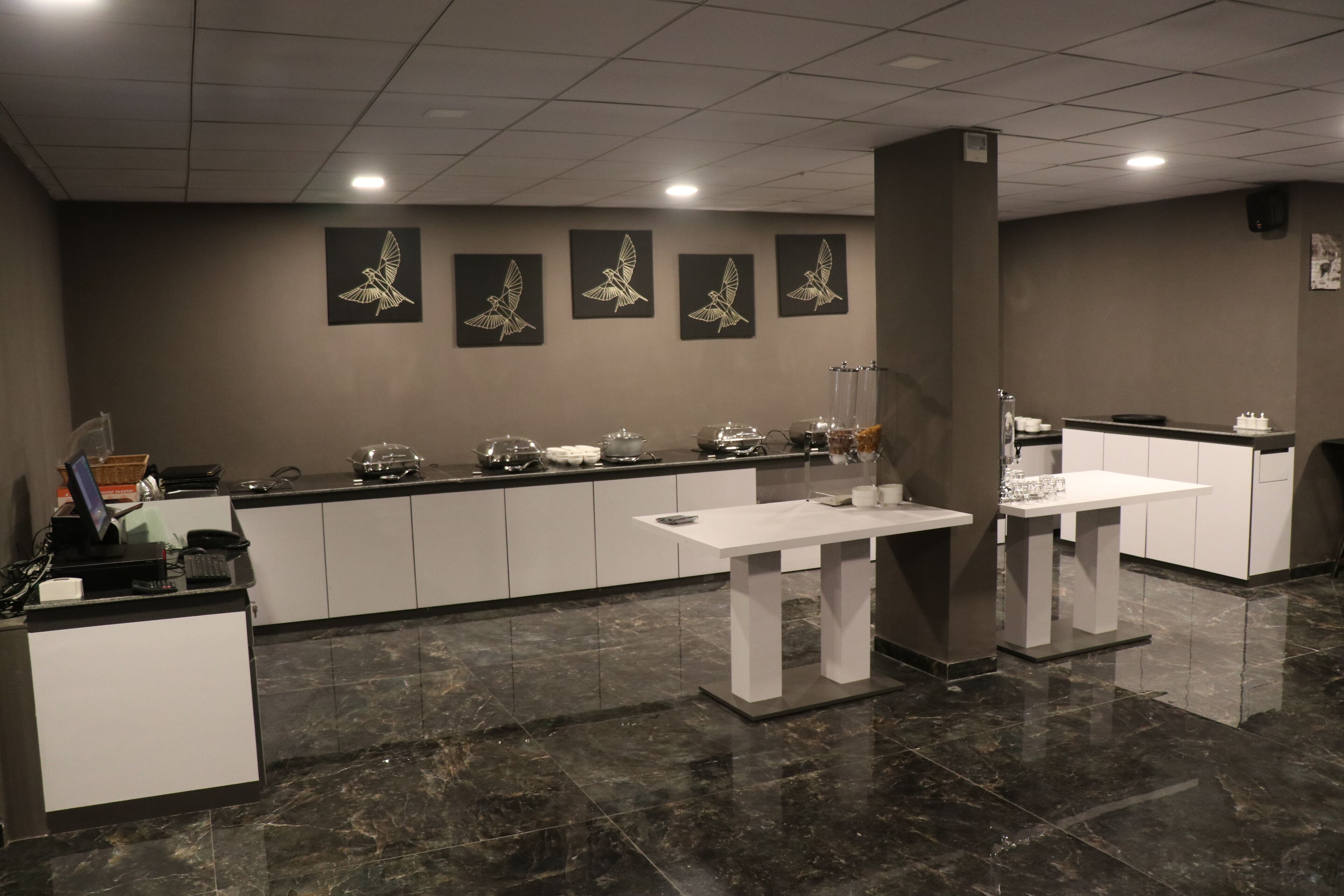 Un moderno vestíbulo de hotel con una mesa de recepción, una zona de estar con una mesa blanca y un mostrador con dispensadores de comida y bebida.