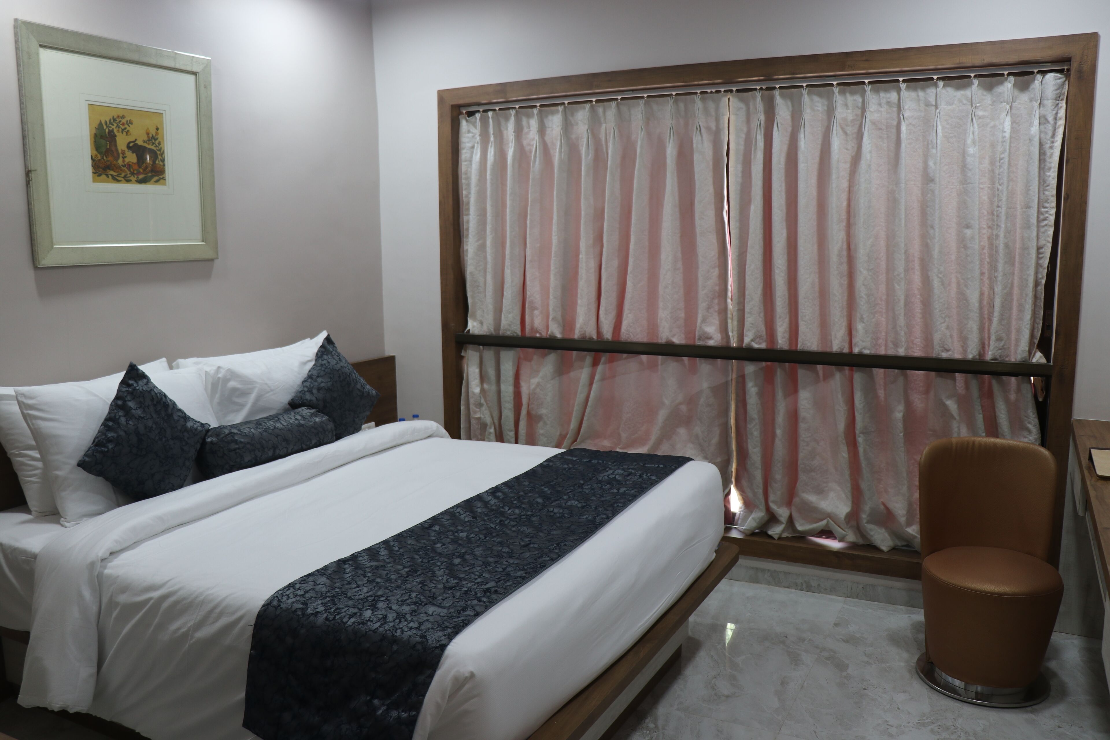 A neatly made bed with a dark blue bedspread, a wooden headboard, and a brown chair beside it.