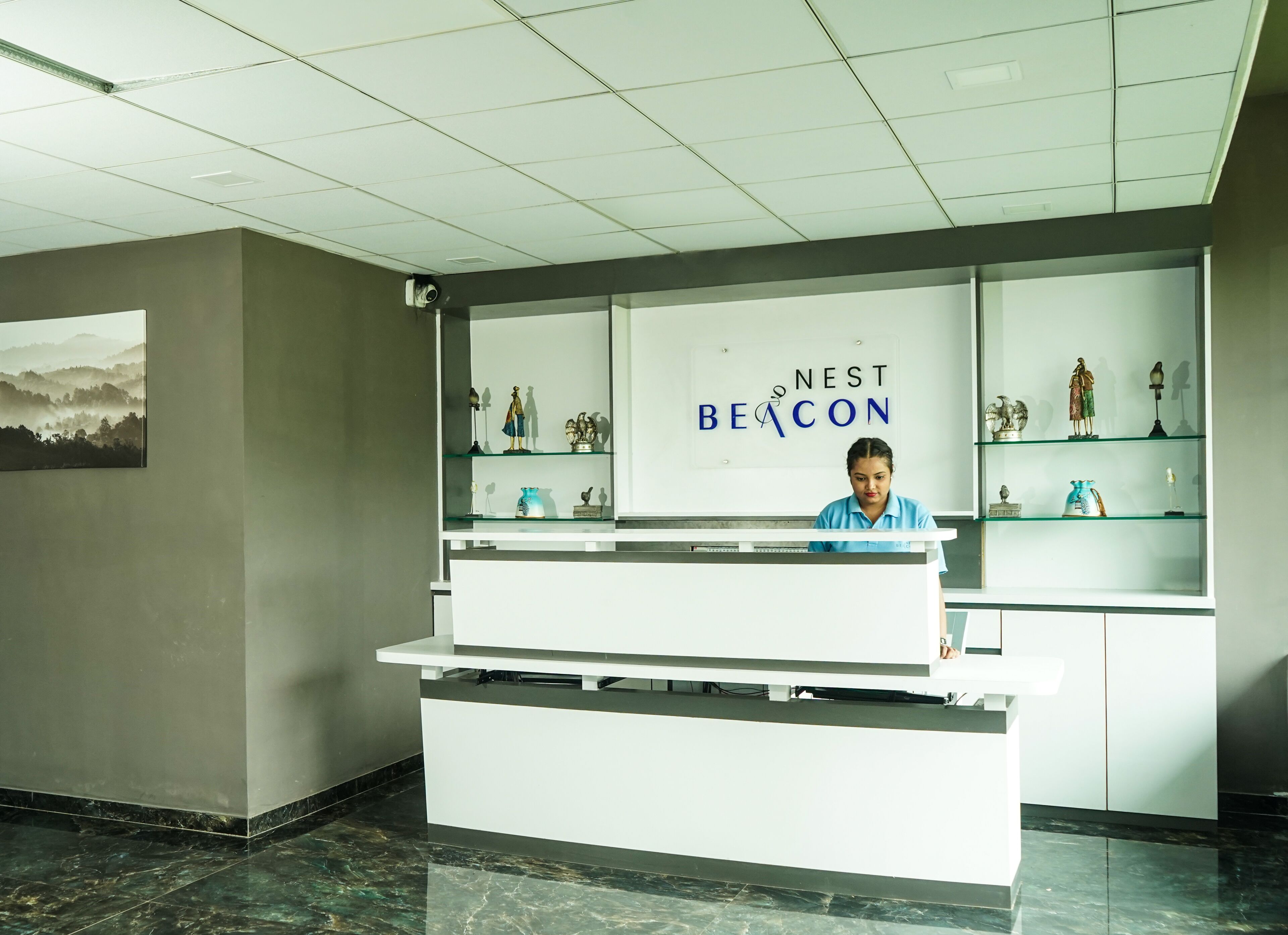 Un mostrador de recepción con un letrero que dice "NEST BEACON" y una recepcionista. Hay estantes de vidrio con diversos objetos.