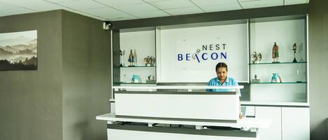 A reception desk with a sign reading "NEST BEACON" and a receptionist. There are glass display shelves with various items.