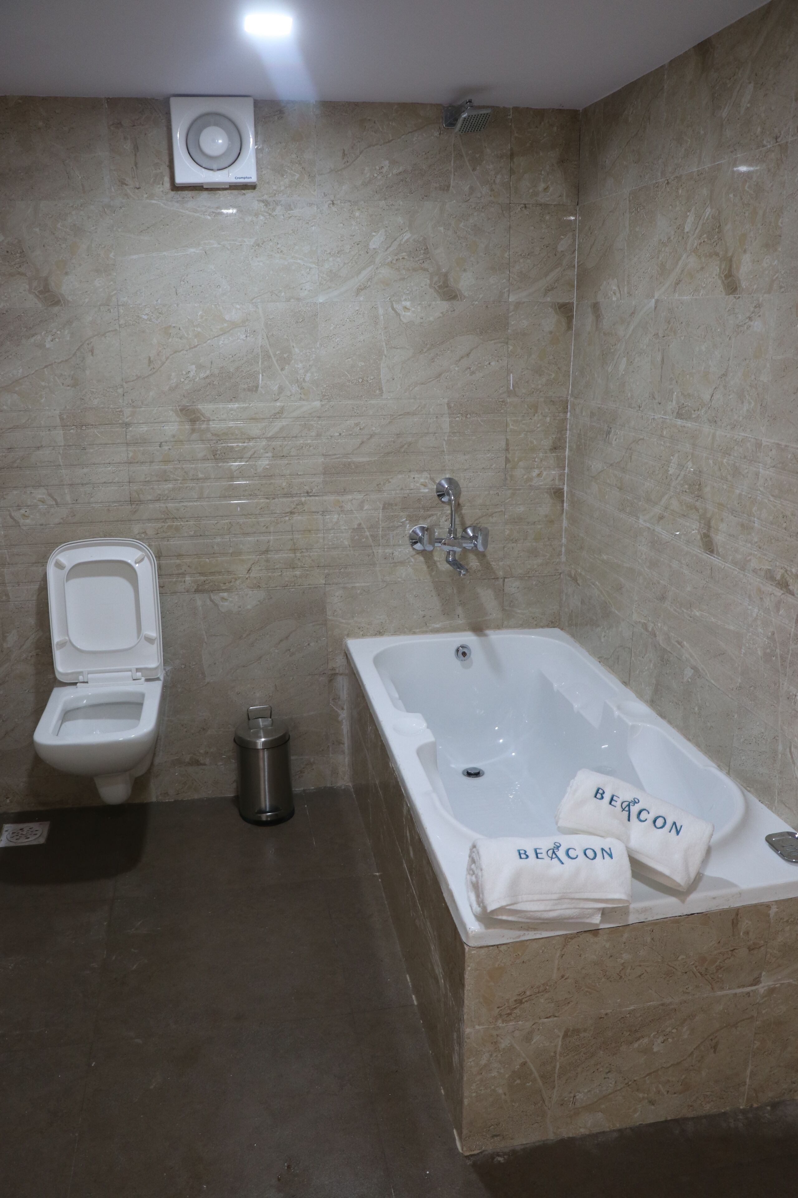 Ein Badezimmer mit Toilette, Mülleimer und einer Badewanne mit Handtüchern, die mit "Beacon" beschriftet sind.