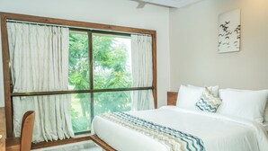 Un dormitorio con un ventanal grande, una cama con ropa de cama blanca y vistas al exterior con vegetación.