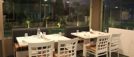 A restaurant with white tables and chairs, a marble floor, and a view of trees and a building through large windows.