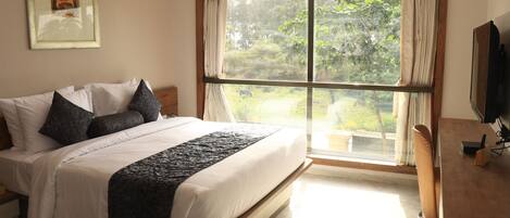 Un dormitorio con una cama grande, un escritorio, un televisor y una ventana con cortinas.