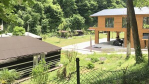 Une cabane rustique avec un toit en métal, entourée d’une végétation luxuriante, et un bâtiment en bois doté d’un porche.