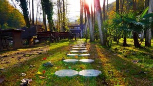 Un chemin de pierres qui traverse un jardin planté d’arbres et mène à un petit bâtiment.
