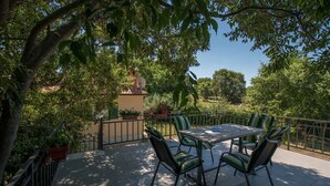 Une terrasse extérieure avec une table et des chaises, entourée de verdure et offrant une vue sur un bâtiment en arrière-plan.