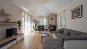 Un salon moderne doté d’un téléviseur à écran plat, d’un canapé gris, d’une table basse en bois et d’un coin repas avec une table et des chaises.