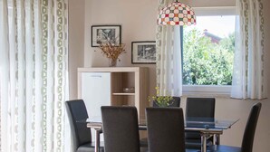 Un coin repas comprenant une table et quatre chaises, un buffet et une fenêtre avec des rideaux.
