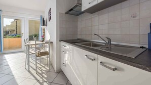 A modern kitchen with white cabinets, a stainless steel sink, and a dining area with a table and chairs. - Holiday apartment with air conditioning near the sea (Lovrečica)