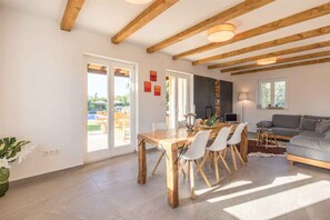 Un salon moderne avec une table à manger en bois, des chaises blanches, un canapé gris et un téléviseur.