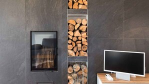 Ein modernes Wohnzimmer mit Kamin, Fernseher und einer an der Wand befestigten Holzregal mit gestapeltem Brennholz.