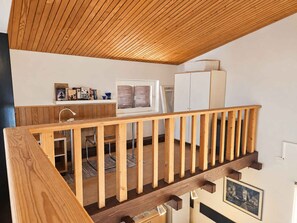 Una escalera de madera que conduce a un dormitorio en loft con un escritorio, una silla y libros.