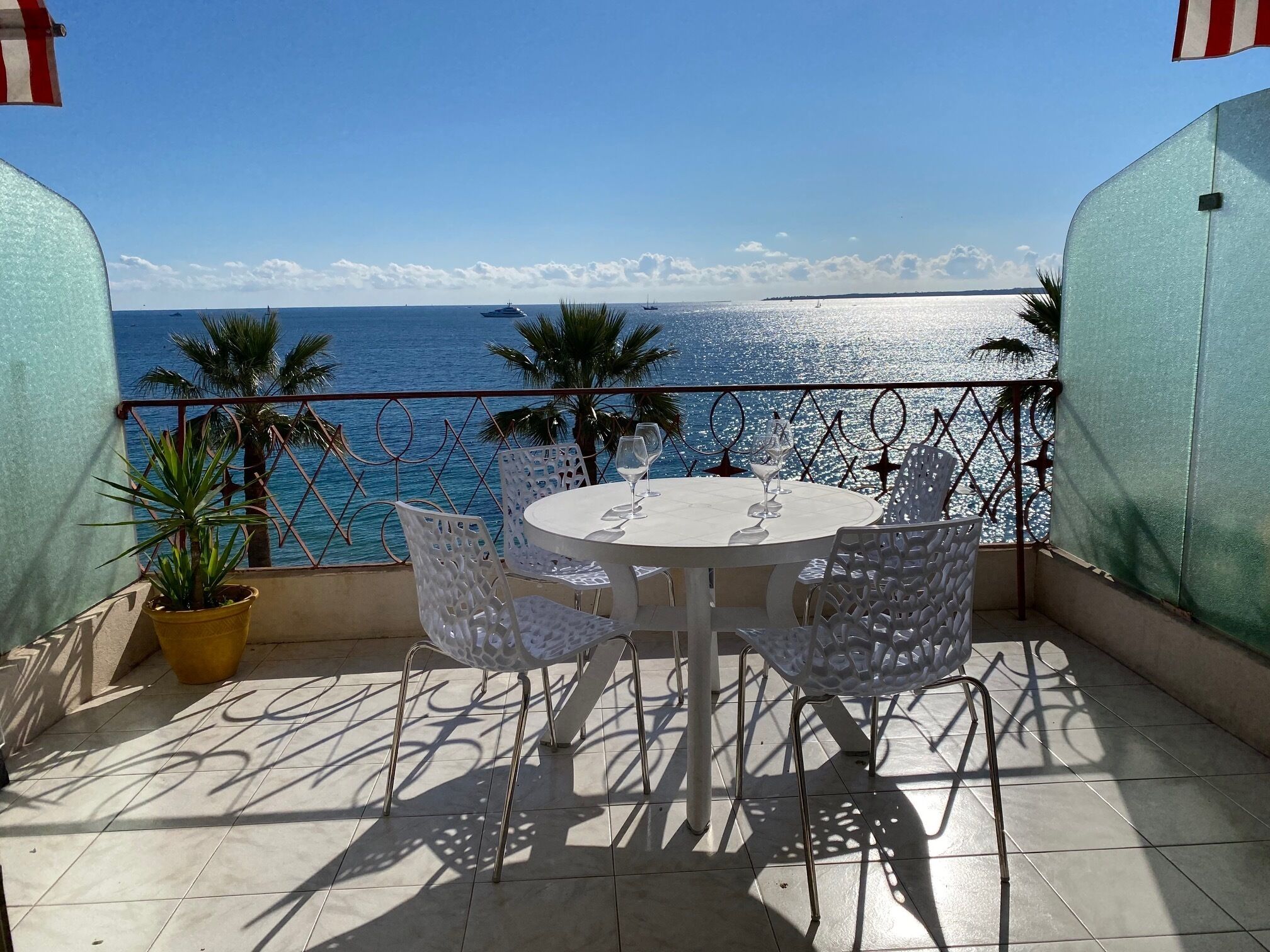 Une table ronde entourée de chaises, sur un balcon donnant sur la mer.