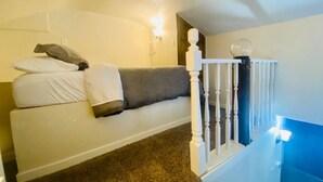 A room with a white sofa, a white railing, and a carpeted floor. - The Tiny Piney Loft - Live. Work. Play. Downtown Green Bay! (Green Bay)