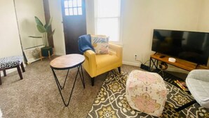 A living room with a yellow armchair, a round coffee table, a flat-screen TV, and a patterned rug. - The Tiny Piney Loft - Live. Work. Play. Downtown Green Bay! (Green Bay)