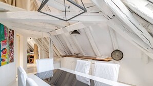 A small, rustic attic room with a slanted ceiling, a wooden table, and a hanging light fixture.