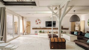 A spacious living room with a large window, a wooden bench, a sofa, and a TV mounted on the wall.