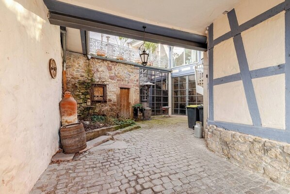 A cobblestone courtyard with stone walls, a wooden barrel, and a metal lantern.