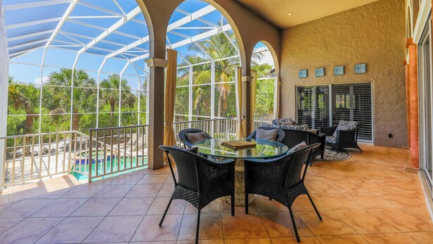 A spacious patio with a glass table and chairs, overlooking a pool and palm trees. - STARFISH OASIS - NEW TO RENTALS! (Sanibel)