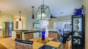 A modern kitchen with stainless steel appliances, a dining area with wicker chairs, and a large window offering a view of the city. - STARFISH OASIS - NEW TO RENTALS! (Sanibel)