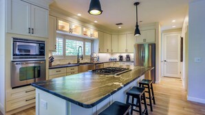 A modern kitchen with stainless steel appliances, a large island with bar stools, and pendant lighting. - STARFISH OASIS - NEW TO RENTALS! (Sanibel)
