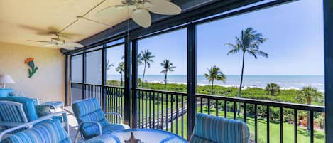 A balcony with a glass table, striped chairs, and a ceiling fan.